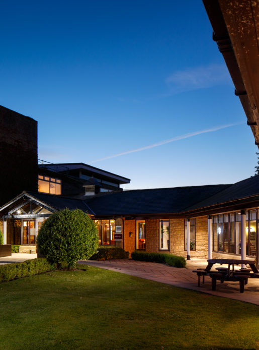 Exterior shot of Mercure Wetherby Hotel at dusk, patio area light up, lawn