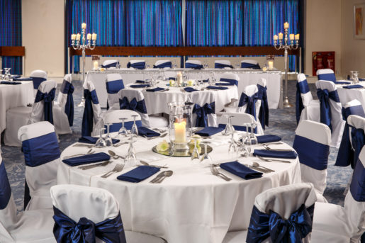 The Harewood Suite at Mercure Wetherby Hotel set up for a wedding breakfast, white linen, navy blue sashes, candles