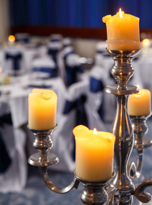 The Harewood Suite at Mercure Wetherby Hotel set up for a wedding breakfast, white linen, navy blue sashes, close up of silver candlestick